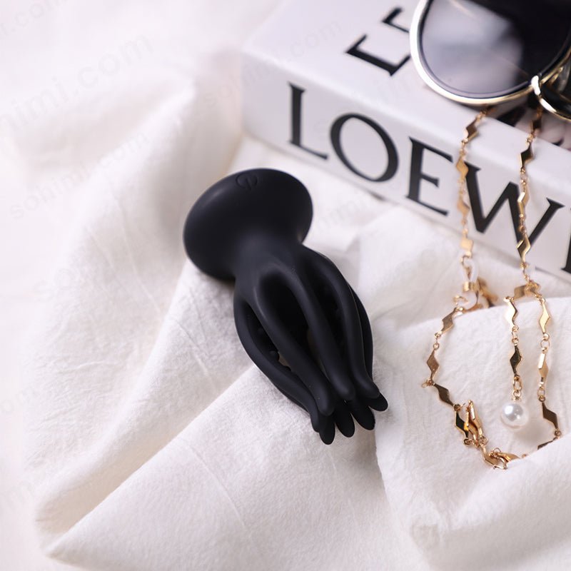 Black silicone penis trainer on a white surface with jewelry in the background