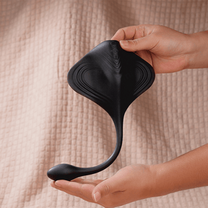 Black silicone product held by a hand on a beige textured background