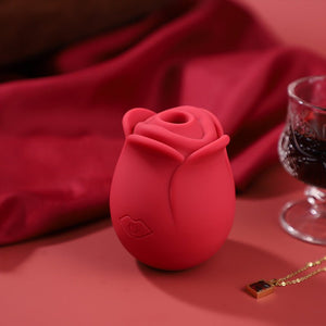 Red rose-shaped vibrator on a red surface with a glass of wine and necklace.